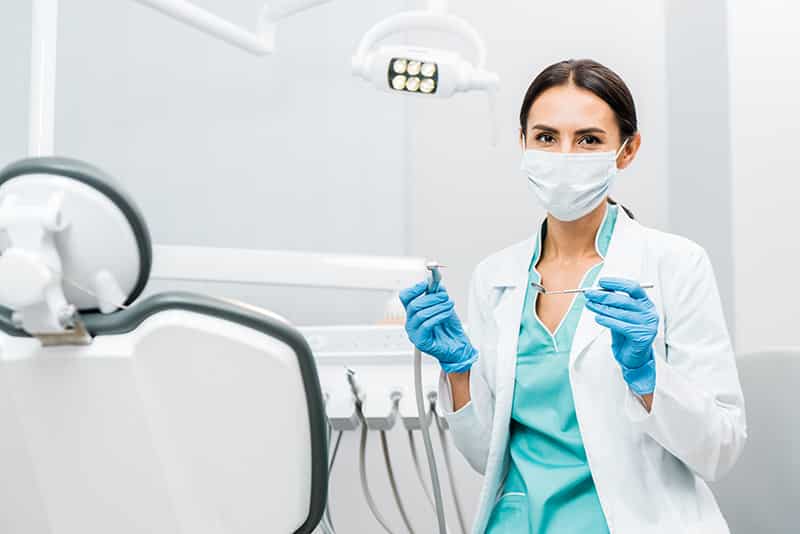 hygienist wearing mask holds dental tools - dentistry tech solutions