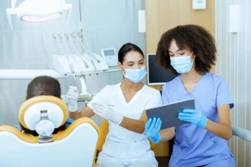 A dentist and an assistant looking at dental technology to asses a patient sitting on a chair.